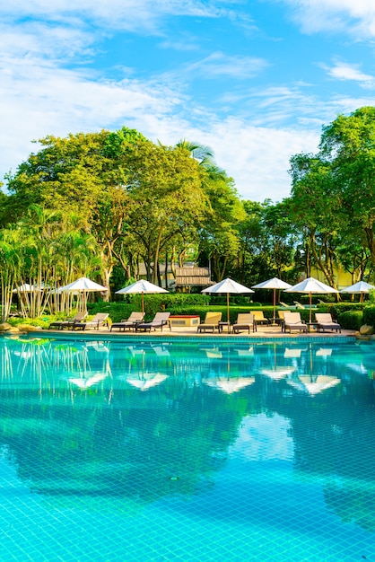 Bellissimo ombrellone e sedia di lusso intorno alla piscina all'aperto in hotel e resort con palme da cocco