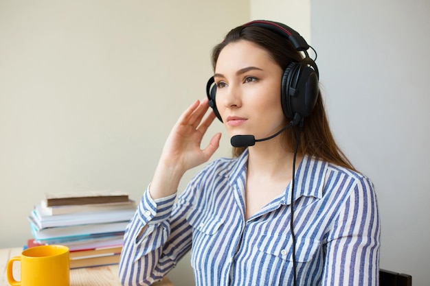 Bellissimo operatore freelance che lavora nel marketing online con cuffie e un laptop in un desktop in ufficio. Donna attenta del call center che lavora da casa parlando con il cliente