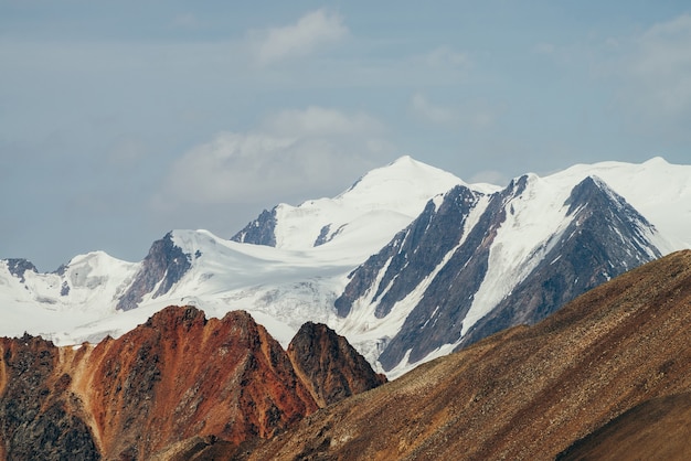 Bellissimo paesaggio alpino minimalista con un'enorme montagna innevata dietro un muro scosceso rosso appuntito.