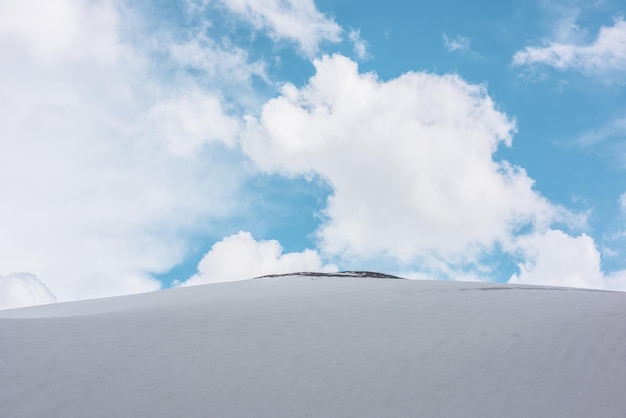 Bellissimo paesaggio con enorme cupola di montagna innevata con cima rocciosa sotto grandi e lussureggianti nuvole bianche nel cielo blu Incredibile scenario di montagna con alta montagna di neve a forma di cupola al centro con tempo variabile