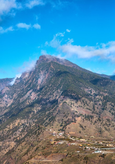 Bellissimo paesaggio della cima di una montagna vicino a una piccola città o villaggio Vista tranquilla e panoramica di una vetta con uno sfondo di cielo blu nuvoloso in una giornata estiva Una vetta con piante verdi e natura lussureggianti