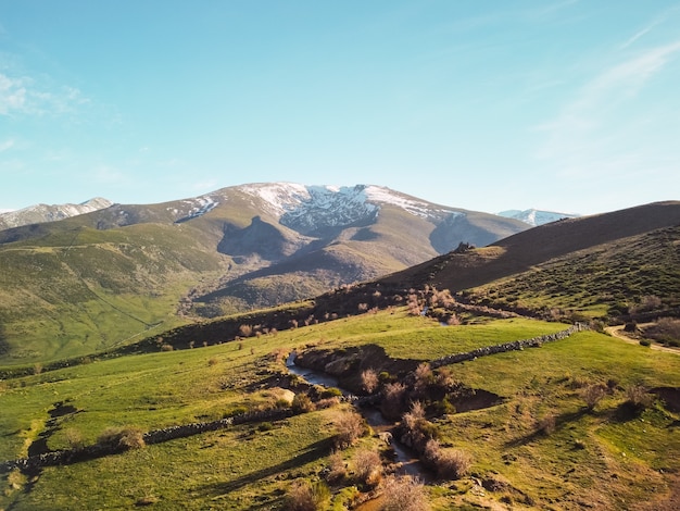 Bellissimo paesaggio di campagna con prati e montagne ricoperte di montagna verde e innevata in una giornata di sole