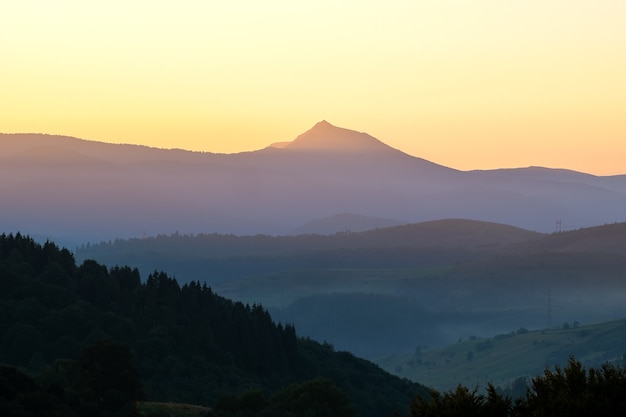 Bellissimo paesaggio di montagna con cime nebbiose e valle nebbiosa al tramonto.