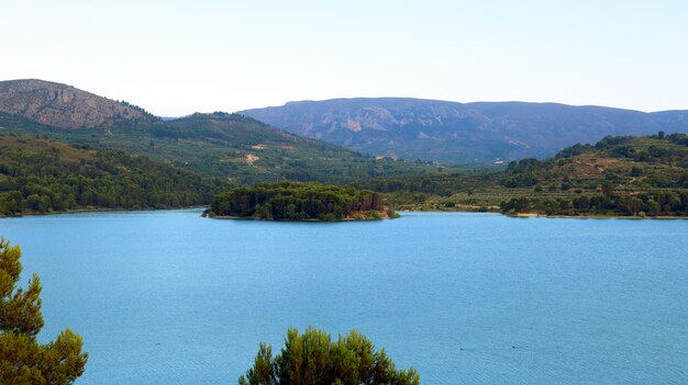 Bellissimo paesaggio, grande lago artificiale in montagna, acqua molto blu, alberi di pino sulla riva, isola