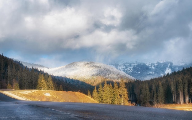 Bellissimo paesaggio invernale con montagne alberi strada e cielo nuvoloso