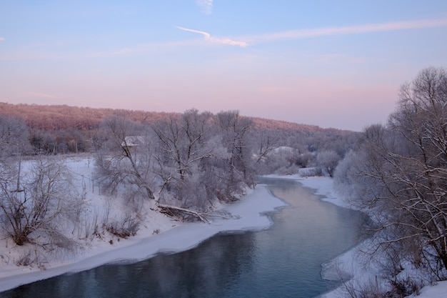 Bellissimo paesaggio invernale con vista sul fiume tortuoso all'alba e sulle rive della neve