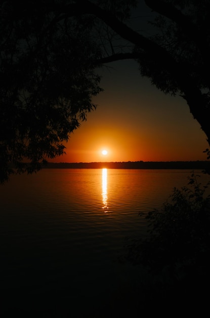 Bellissimo paesaggio naturale tramonto arancione sul lago in cornice di alberi Sole e riflesso sull'acqua vignetta