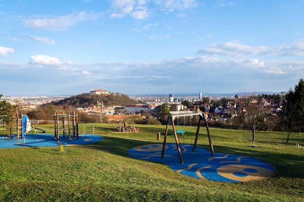 Bellissimo parco giochi con altalena in legno e strutture per l'arrampicata per bambini con il castello di Spilberk sullo sfondo Brno Moravia Repubblica Ceca giornata di sole