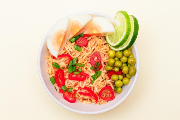 Bellissimo piatto di noodle con uova di piselli verdi peperoncino e lime su sfondo bianco spaghetti istantanei vista dall'alto