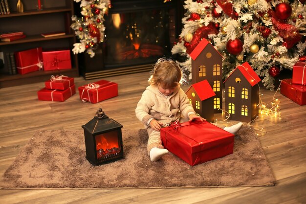 bellissimo ragazzo dai capelli ricci in un abito invernale a maglia tiene una scatola regalo di Natale Capodanno