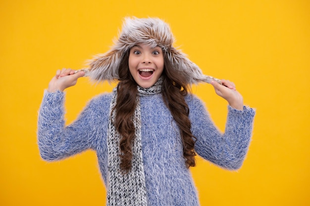 Bellissimo ritratto di bambini d'inverno Ragazza adolescente in posa con maglione invernale e cappello in maglia su sfondo giallo Ragazza adolescente eccitata