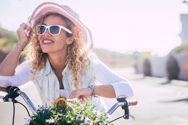 Bellissimo ritratto di donna caucasica con capelli ricci e cappello che si gode un giro in bicicletta