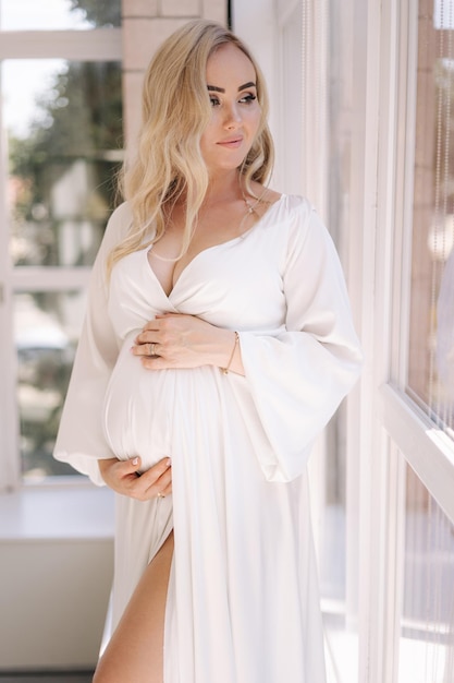 Bellissimo ritratto di donna incinta in abito bianco concetto di donna incinta perfetta le mise la mano