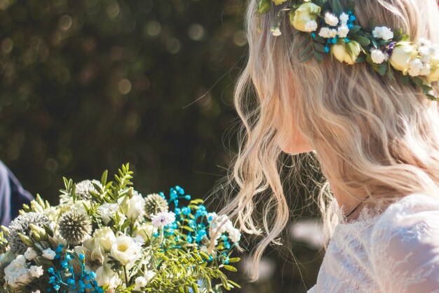 Bellissimo ritratto di sposa con bouquet di fiori e ghirlanda sulla testa in abito da sposa bianco all'aperto