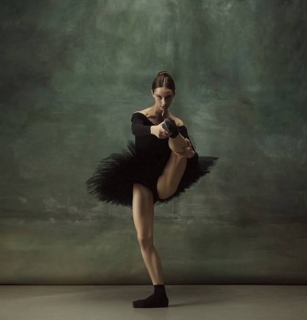 Bellissimo ritratto. Graziosa ballerina classica che balla, posa isolata su sfondo scuro studio. Tutù nero di eleganza. Grazia, movimento, azione e concetto di movimento. Sembra senza peso. Alla moda.