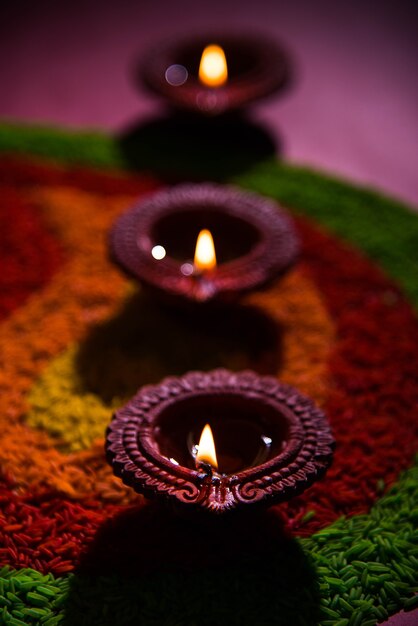 Bellissimo saluto Diwali usando Diya o lampada ad olio di argilla accesa e disposta su Rangoli fatta da chicchi di riso multicolori, messa a fuoco selettiva