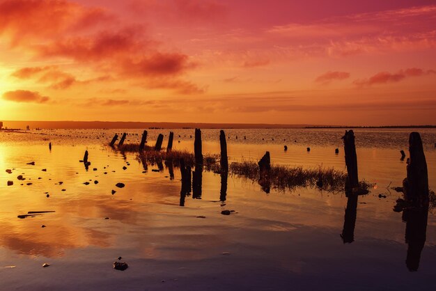 Bellissimo tramonto colorato rosso soleggiato sul lago con pietre perni in legno e riflessione sullo sfondo naturale stagionale delle vacanze estive