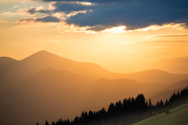 Bellissimo tramonto drammatico in montagna. Paesaggio con il sole che splende attraverso le nuvole arancioni