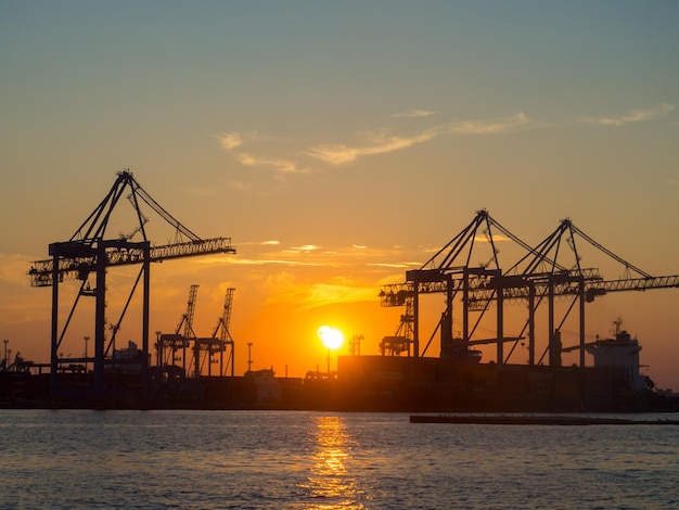 Bellissimo tramonto sopra il porto all'ora del tramonto con sagome di gru da carico Porto industriale del Mar Nero Odesa Ucraina con molte gru cabine scatole e serbatoi vicino all'acqua sul tramonto colorato