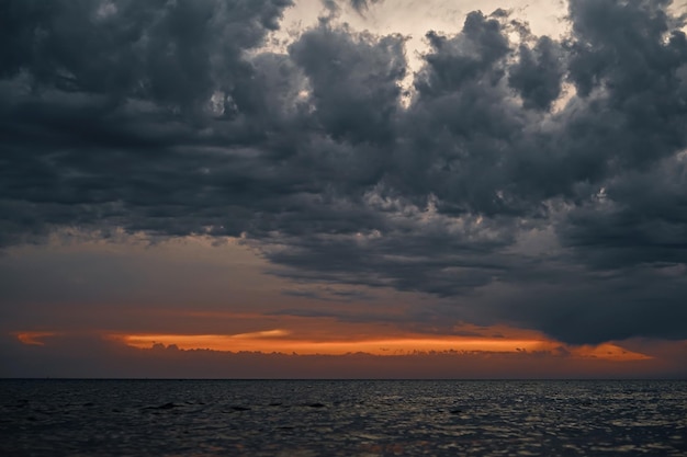 Bellissimo tramonto sul mare con nuvole drammatiche grigie e cielo drammatico con strisce di tramonto arancione