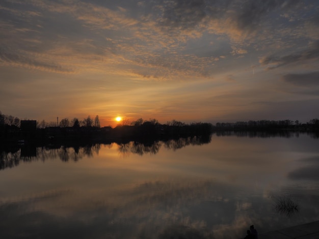 Bellissimo tramonto sull'acqua Riva e orizzonte del fiume Le nuvole luminose sono dipinte dal sole della sera Il sole discendente Cielo e nuvole drammatici grigio arancione giallo