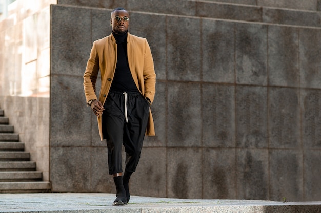 Bellissimo uomo di colore in abiti eleganti che cammina con le mani in tasca. Stile di vita urbano.