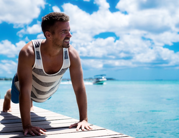 Bellissimo uomo muscoloso che si esercita in riva all'oceano. Il fitness all'aperto estivo ti rende sexy e abbronzato.