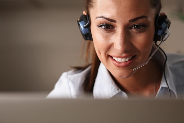 Bello agente sorridente del call center con l'auricolare che comunica con un cliente al telefono