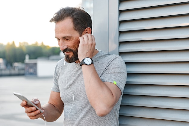 Bello allegro forte sportivo maturo ascoltando musica con gli auricolari utilizzando il telefono cellulare.