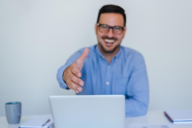 Bello allegro sorridente giovane imprenditore imprenditore manager o socio in affari che offre la mano per la stretta di mano in ufficio dà la mano per la stretta di mano propone partnership guardando direttamente la fotocamera