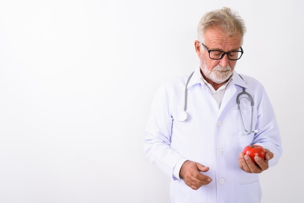 bello anziano uomo barbuto medico guardando il pomodoro rosso mentre si indossano occhiali su bianco