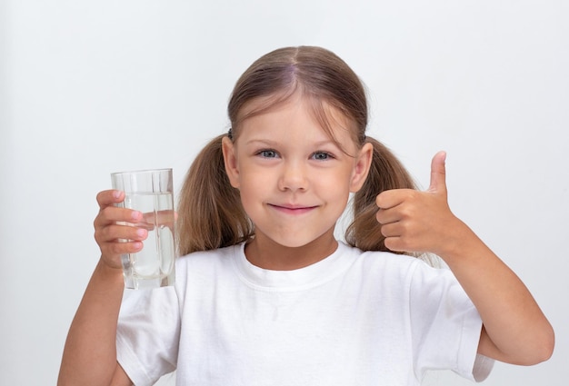 Bello bambino caucasico che tiene un bicchiere di acqua pura che guarda l'obbiettivo su sfondo bianco