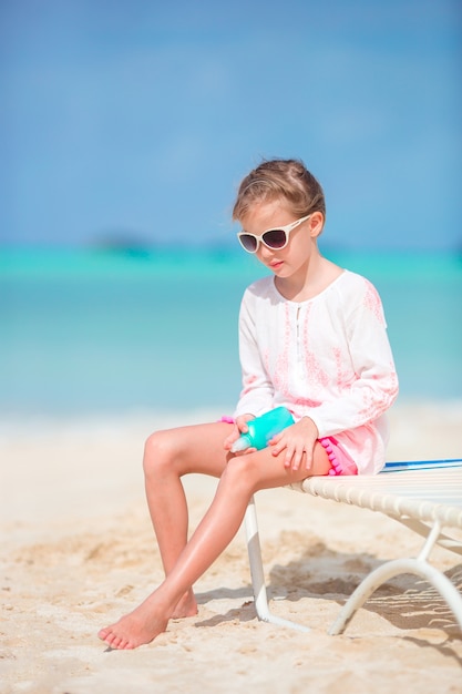 Bello bambino con la bottiglia di crema solare sulla spiaggia tropicale