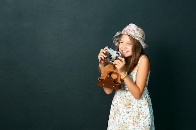 Bello bambino sorridente (ragazza) con i denti bianchi che tengono una macchina fotografica istantanea