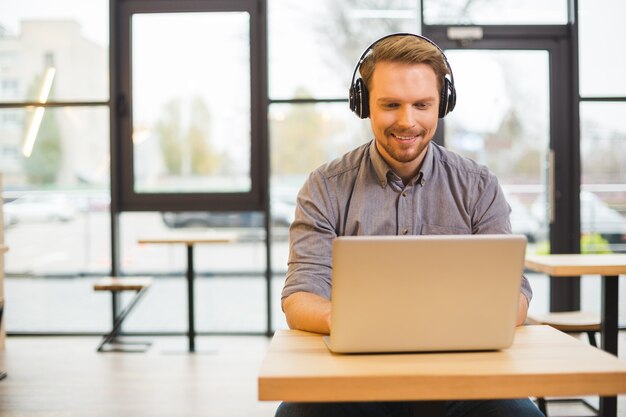 Bello bello allegro uomo seduto al computer portatile e indossa le cuffie mentre si lavora