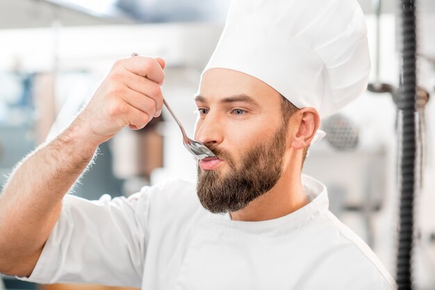 Bello chef che assaggia il cibo al cucchiaio nella bellissima cucina del ristorante