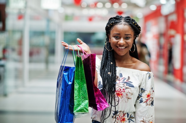Bello cliente afroamericano ben vestito della donna con i sacchetti della spesa colorati al centro commerciale.