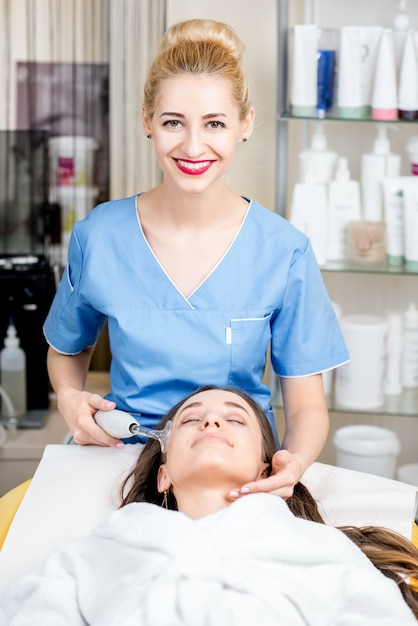 Bello cosmetologo in uniforme che fa un trattamento facciale al paziente nell'ufficio di cosmetologia