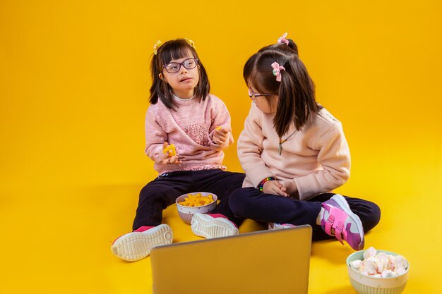 Bello e gentile. Piccoli gemelli adorabili che si siedono sul pavimento nudo con marshmallow e patatine mentre guardano film sul computer portatile