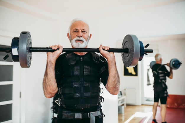 Bello e positivo uomo anziano che fa esercizi in tuta di stimolazione muscolare elettrica.