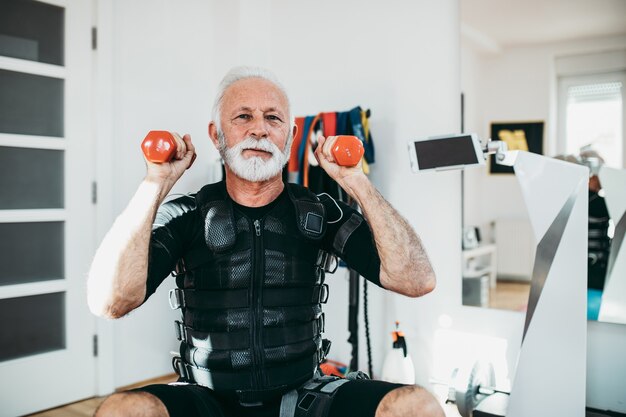 Bello e positivo uomo anziano che fa esercizi in tuta di stimolazione muscolare elettrica.