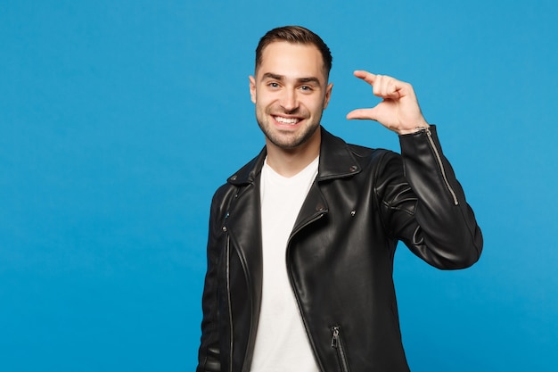 Bello elegante giovane uomo con la barba lunga in giacca di pelle nera t-shirt bianca che guarda macchina fotografica isolata sul ritratto dello studio del fondo della parete blu. Concetto di stile di vita di emozioni sincere della gente. Mock up copia spazio