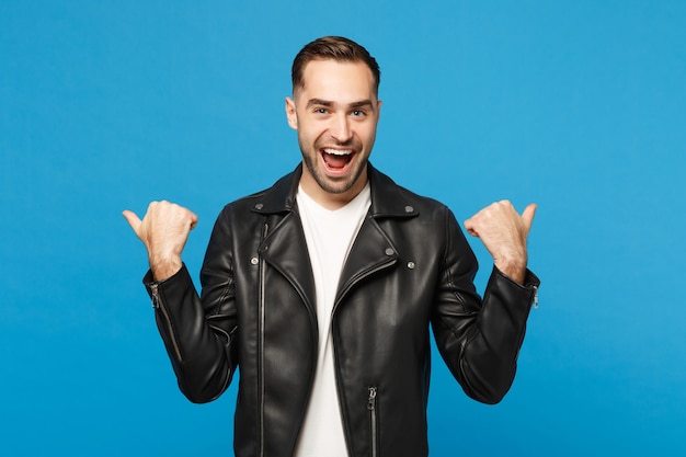 Bello elegante giovane uomo con la barba lunga in giacca nera t-shirt bianca che mostra sull'area di lavoro isolata sul ritratto in studio di sfondo blu parete. Concetto di stile di vita di emozioni sincere della gente. Mock up copia spazio.