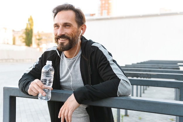 Bello forte sportivo maturo tenendo la bottiglia con acqua.