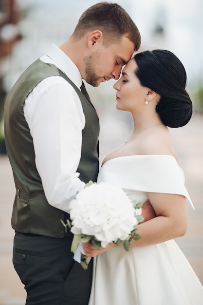 Bello forte sposo abbracci con la sua giovane bella sposa in abito bianco con un mazzo di fiori bianchi