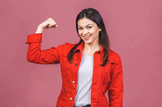 Bello giovane bicipite sorridente della flessione della donna isolato sulla parete rosa.