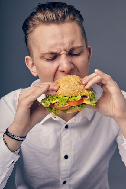 Bello giovane che mangia un hamburger fresco