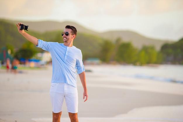 Bello giovane che prende se stessa una foto di auto sulla spiaggia tropicale