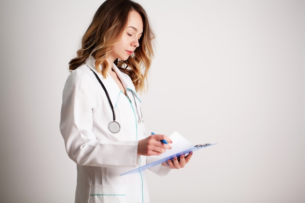 Bello giovane medico femminile nelle camice che guarda la carta di un paziente