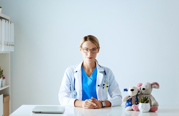 Bello giovane medico femminile sorridente che si siede allo scrittorio.